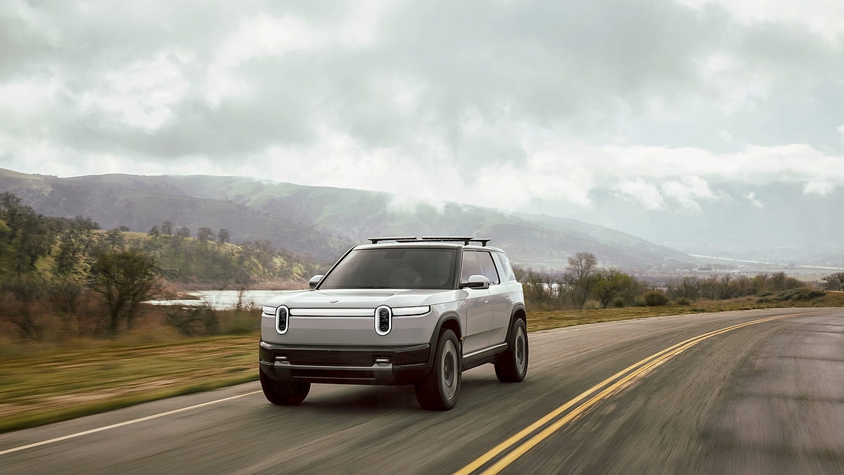 Rivian R2S electric SUV driving on a road with mountains and clouds in the background